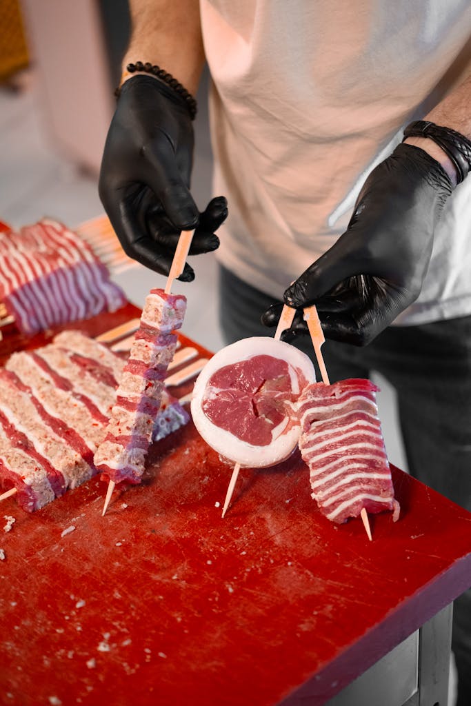 Close-up of a chef arranging skewered meats on a red cutting board, showcasing fresh cuts.