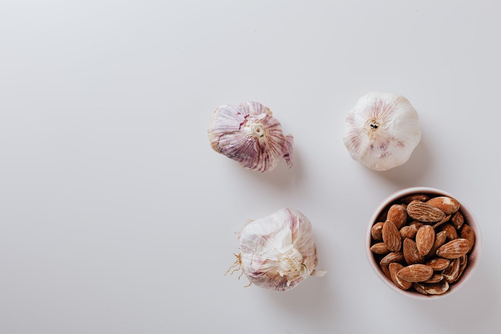 Overhead shot of garlic bulbs and almonds on a white surface with ample copy space.