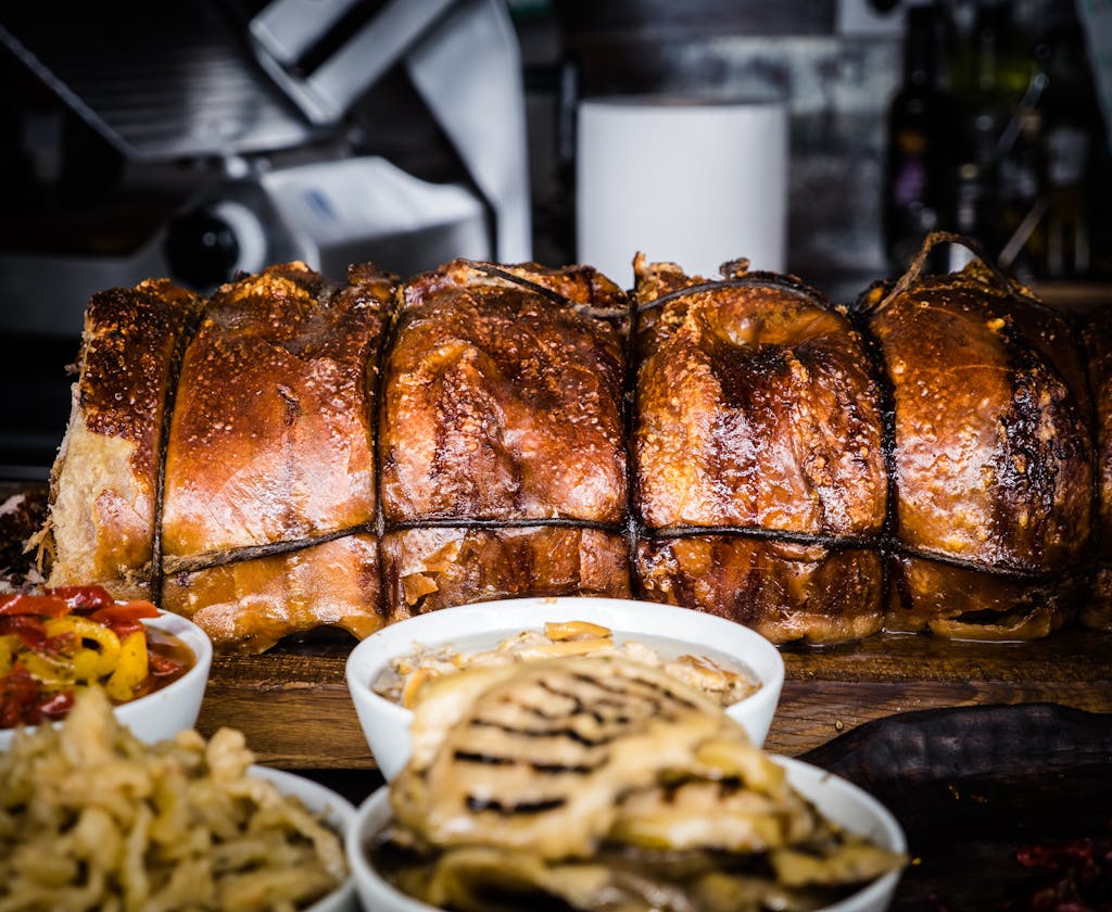Close-up of traditional Italian porchetta with side dishes, showcasing rich textures and flavors.